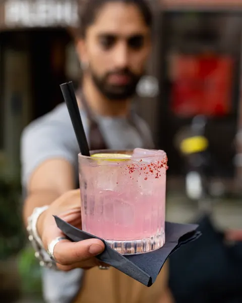 Shawn rækker en lyserød drink med rød kant frem mod kameraet