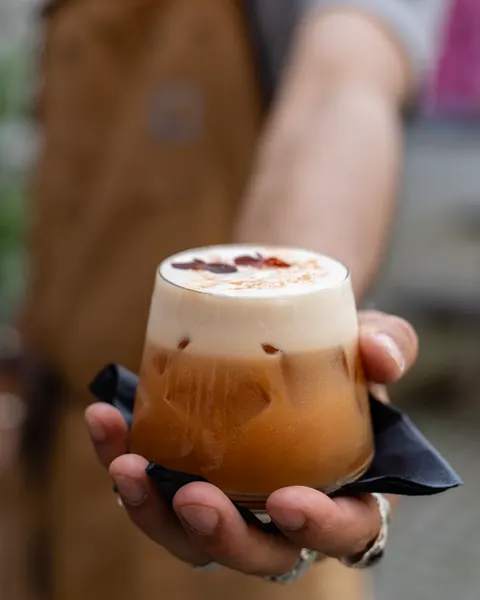 En cocktail med tykt skum og tørrede blomster serveres på en sort serviet